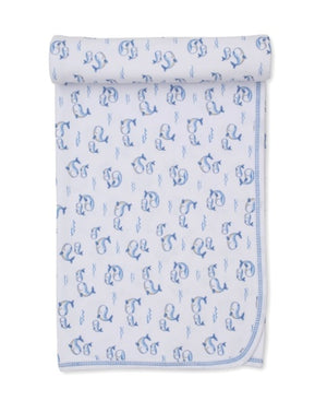 Kissy Kissy Whale Pods Blanket—white Pima cotton baby blanket featuring blue embroidered letters and charming whale designs, rolled at the top and neatly folded at the corner—a soft and cozy choice perfect for little ones.