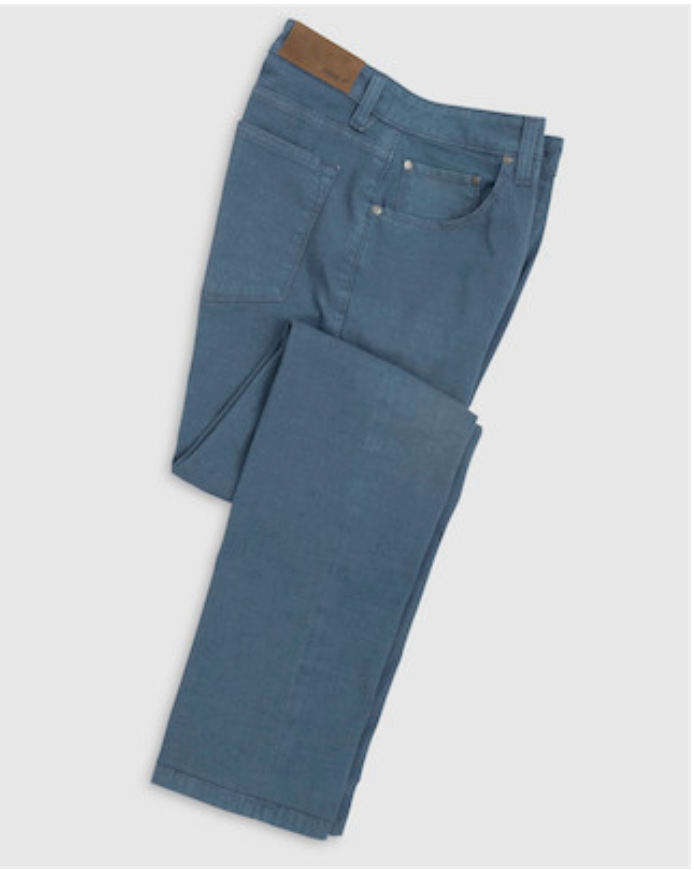 The Johnnie-O Atlas 5-Pocket Pant, made from garment-dyed stretch twill and detailed with a brown waistband patch, is perfect for warm climates. Shown folded in blue on a light grey background.
