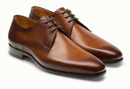The Magnanni Maddin Lace-Up is a pair of brown calfskin leather plain toe derby dress shoes with laces, low heels, and rounded toes from the Línea Flex collection, shown on a white background.
