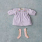 The Louise Misha Baby Girls’ and Girls’ Anette Dress is shown here in lavender corduroy with an embroidered yoke and subtle ric rac details, paired with pink knee-high socks. Both items are laid flat on a textured light blue background.