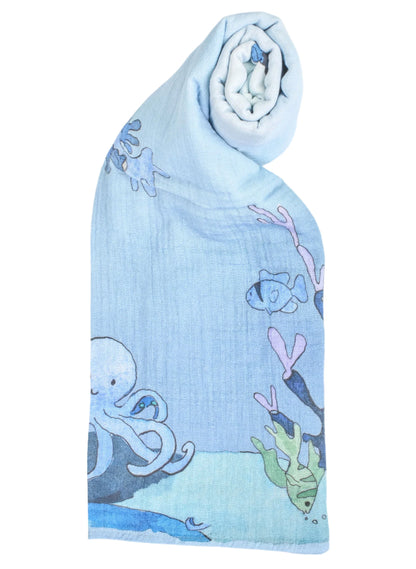 The Timo & Violet Shawl Blanket is a light blue organic cotton muslin baby accessory with octopus, fish, and seaweed illustrations, partially rolled at one end for added coziness.