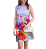 Woman wearing the Lela Rose Kelly Dress, a sleeveless dress with a colorful floral print, holding a white purse. The dress, made from 100% cotton, features a convenient zip closure at the back.