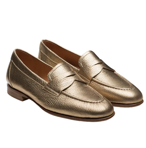 The Sonya Metallic Loafer by Magnanni is a gold leather slip-on featuring an apron toe, supple textured finish, and low wooden heel, shown on a white background.