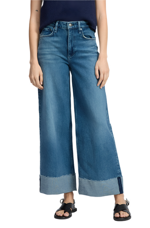 Person wearing Rag & Bone Sofie High Rise Ankle Wide Leg Cuff jeans with a wide-leg blue design and large cuffs, paired with black sandals, standing against a plain background.