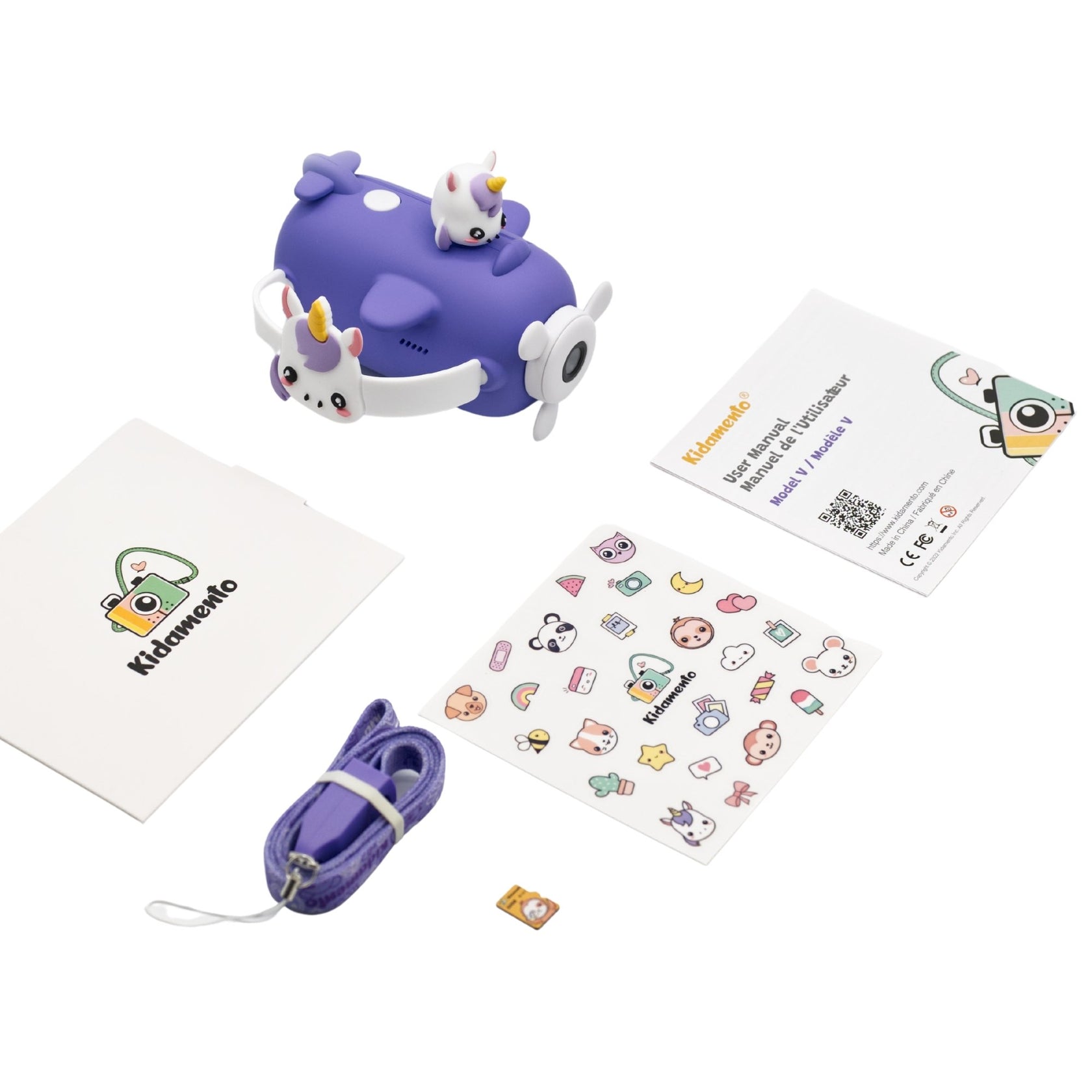 A purple Kidamento Digital Camera Model V, Iris the Unicorn, with unicorn designs, featuring a built-in selfie camera, comes with a matching lanyard, stickers, a small memory card, and informational booklets, all laid out on a white surface.