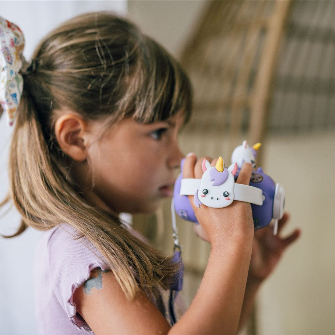 A young girl in a purple shirt looks through a Kidamento Digital Camera Model V, Iris the Unicorn, by Kidamento.