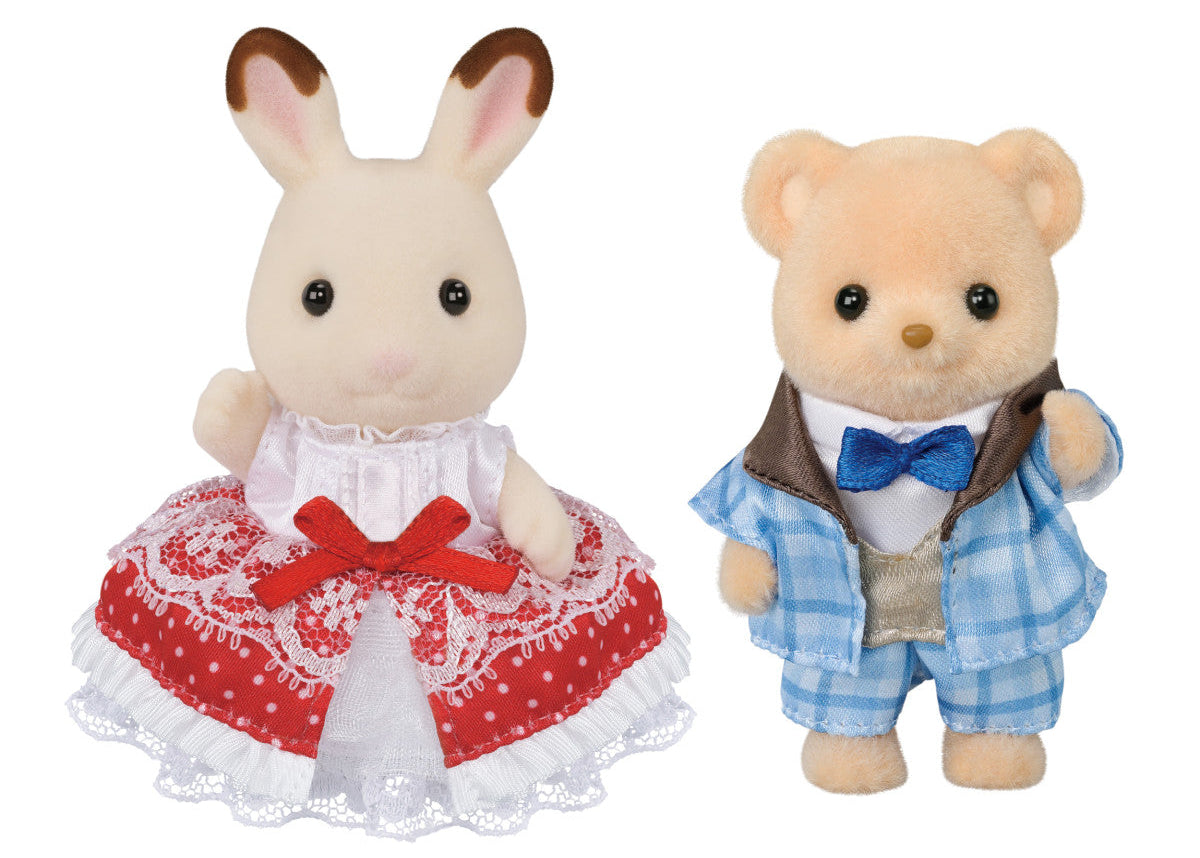 Two plush animal figures from Calico Critters: Freya Chocolate Rabbit in a red and white lace dress and Theo Bear in a blue plaid suit with a bow tie, both standing upright against a white background. The 40th Anniversary Friends – Freya & Theo set features exclusive original outfits, making it a charming collectible for any fan.