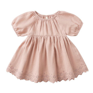 The Quincy Mae Baby Girls' and Girls' Bella Dress is a light pink dress with short sleeves, gathered waist, scalloped hem with eyelet embroidery, round neckline, and a loose fit.