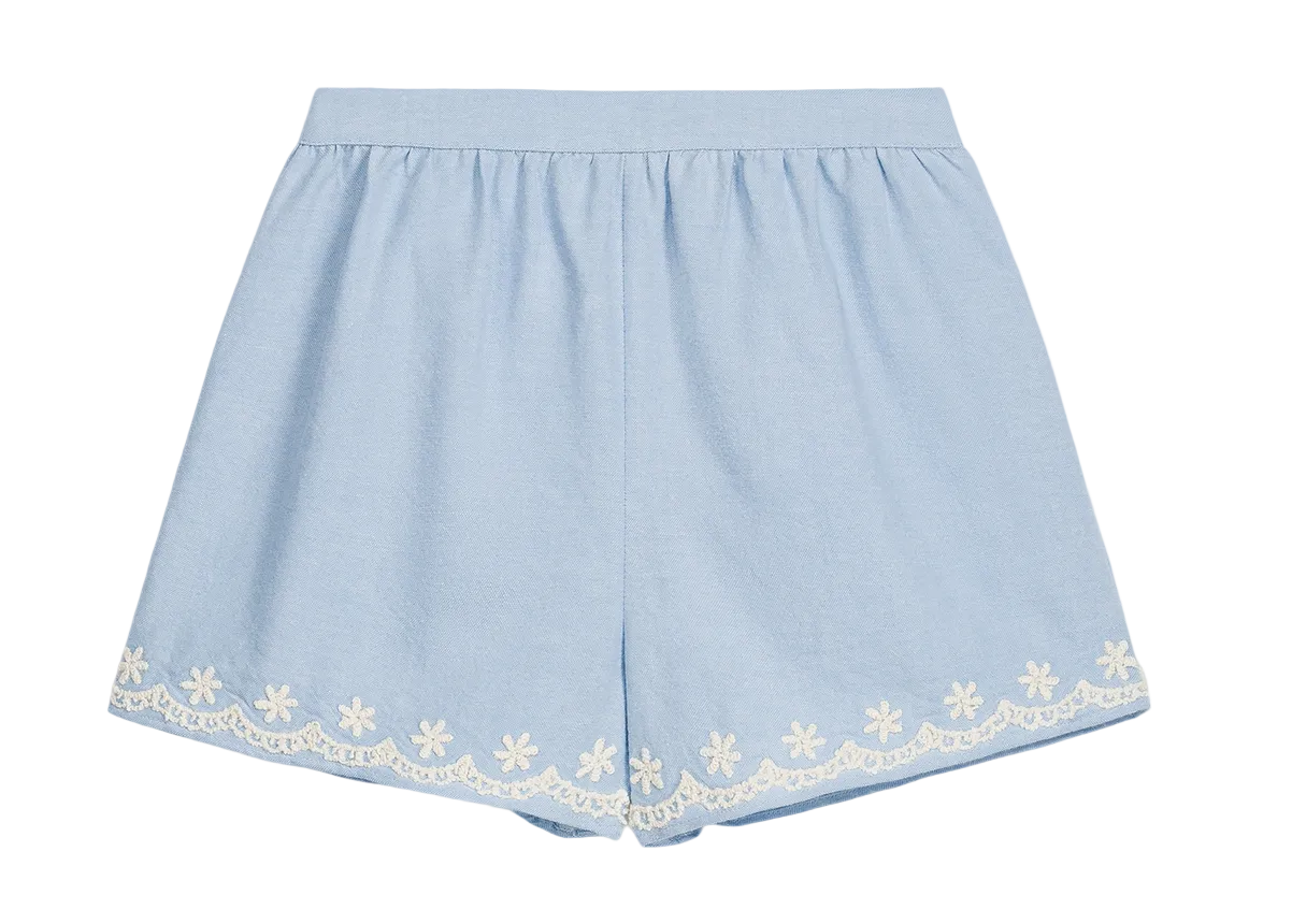 Girls’ Vally Shorts by Louise Misha in light blue Oxford cotton, featuring an elasticized waist and delicate white floral embroidery along the hem, displayed flat on a white background.