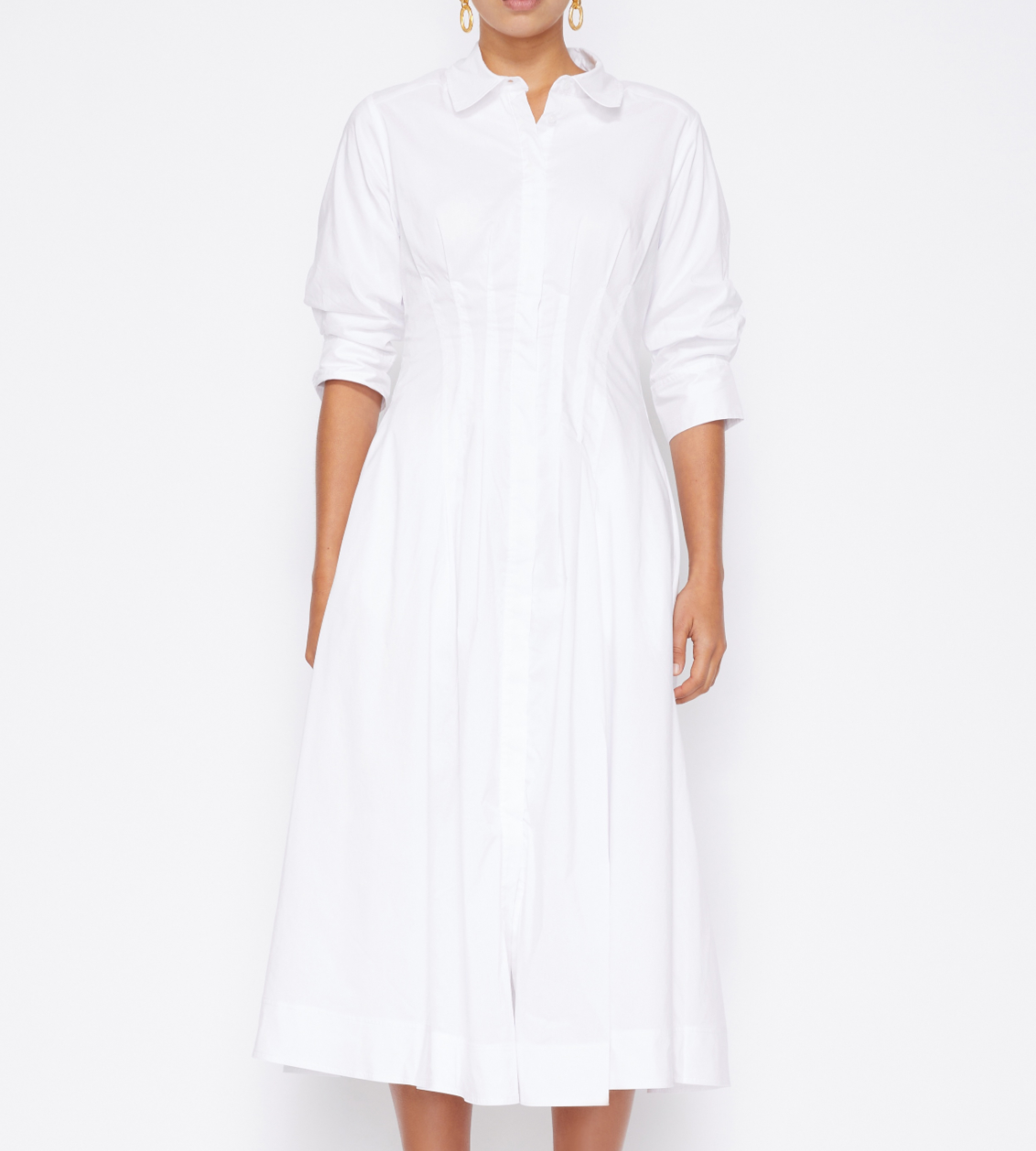 A person wears a white, long-sleeve, button-down Signature Jazz Dress by Simkhai, made from cotton poplin, against a plain background.