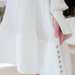 Close-up of a person wearing the Lanvin Flared Pleated Dress with Long Sleeves, made from white crepe de Chine. The sleeve features pleated fabric and pearl buttons, and the person is holding the dress near the buttons to showcase the intricate detailing.