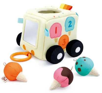 The Hape Ice Cream Activity Cube features a soft toy ice cream truck with a baby-safe mirror, an easy-to-grasp handle, four black wheels, and three detachable plush ice cream cones in orange, brown-pink, and blue placed beside it—perfect for sensory adventures and color matching as little ones explore their favorite ice cream-themed toy.