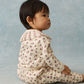 A baby sits on the floor in profile against a light blue background, wearing the Louise Misha Baby Girls’ Rosaline Sweatshirt—a cream-colored floral top featuring a ruffle neckline and decorative collar.
