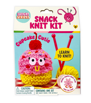 The Bright Stripes Snack Knit Kit - Cupcake Cutie package displays a finished pink and yellow cupcake plush, two red knitting needles, and a ball of yellow yarn. Ideal for beginner knitters, this crafty set features the phrases “Cupcake Cutie” and “Learn to Knit!” on the packaging.