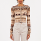 A person wears the Ulla Johnson Liza Cardigan, featuring Fair Isle patterns and a round neckline, with high-waisted light-colored pants, standing against a plain background.