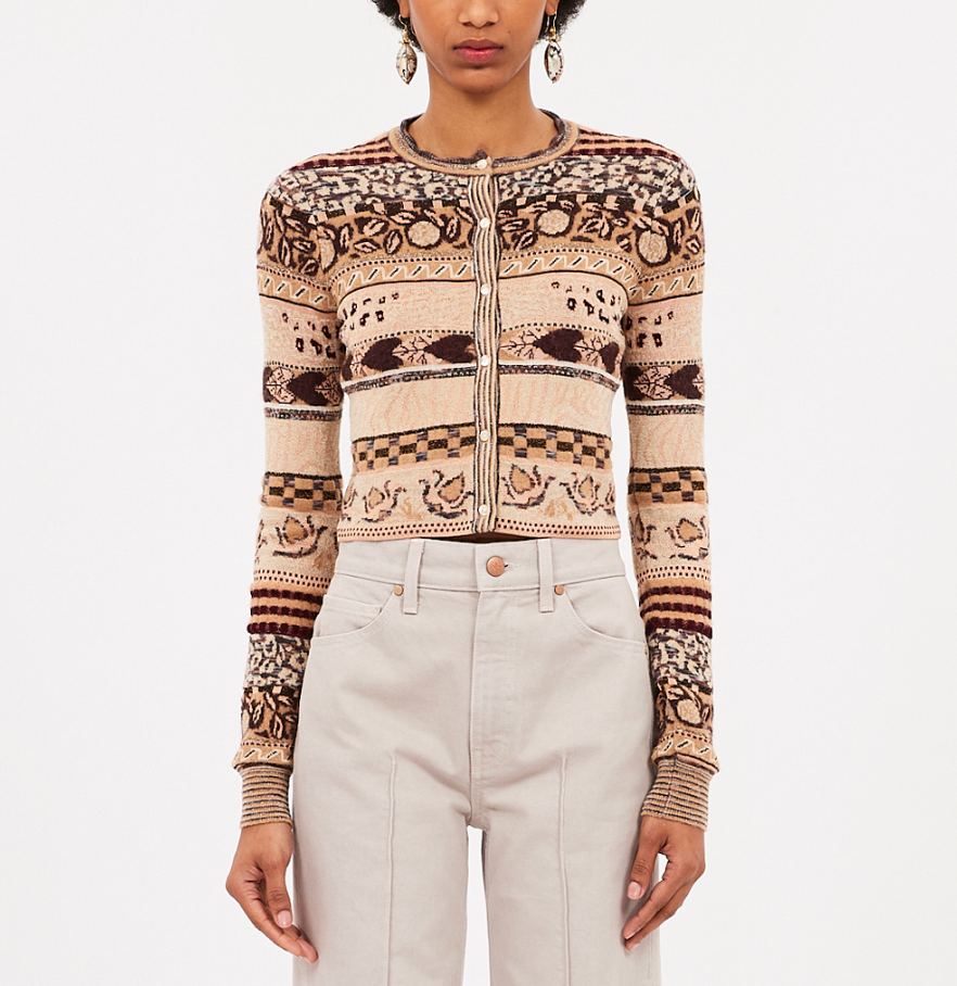 A person wears the Ulla Johnson Liza Cardigan, featuring Fair Isle patterns and a round neckline, with high-waisted light-colored pants, standing against a plain background.