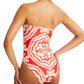 A person is wearing the lemlem Dinha One Piece by Lemlem, a strapless red and white patterned swimsuit with a high-cut leg, facing away.