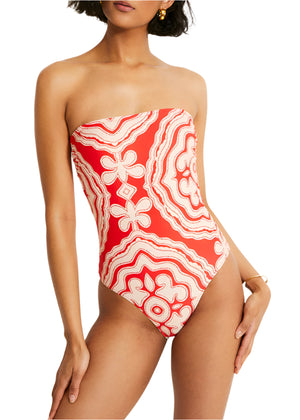 A person is confidently wearing the Lemlem Dinha One Piece by Lemlem, a strapless red and white patterned swimsuit with a sleek neckline that adds elegance.