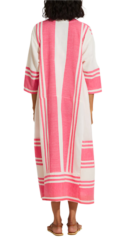 Someone is seen from the back wearing Lemlem’s Fana Caftan, a loose-fitting, long white dress with pink vertical and horizontal stripes made from hand-spun cotton.
