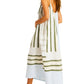 A woman wears the Lemlem Nia Slip Dress, a sleeveless hand-woven cotton piece with green and white stripes, paired with light-colored flats.