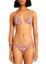 Person wearing Malia Top and Rekka Bottom Bikini by Lemlem, featuring a geometric pattern, adjustable string ties on the triangle top, and string bottoms, stands against a plain white background.