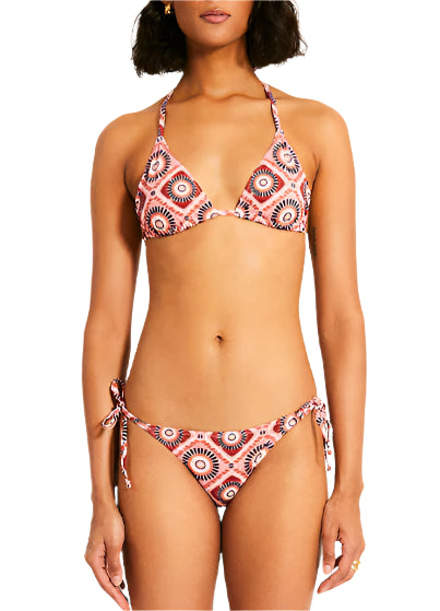 Person wearing Malia Top and Rekka Bottom Bikini by Lemlem, featuring a geometric pattern, adjustable string ties on the triangle top, and string bottoms, stands against a plain white background.
