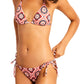 Someone is wearing Lemlem's Malia Top and Rekka Bottom Bikini, showcasing a pink geometric pattern with fashionable string ties for an ideal fit.