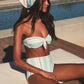 A woman in Lemlem’s Ava Bandeau Top and Elsi High Waist Bottom, paired with a matching headscarf, sits on a lounge chair by the pool.