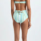 A woman stands barefoot facing away against a plain white background, wearing Lemlem’s Ava Bandeau Top and Elsi High Waist Bottom, a striped ribbed swimsuit with a bandeau top, back tie, and high-waisted bottom.