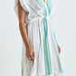A woman models the Lemlem Leila Plunge Dress, a loose-fitting white maxi with blue and green stripes, hand-woven cotton, deep V-neck, and gathered waist detail.