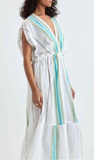 A woman models the Lemlem Leila Plunge Dress, a loose-fitting white maxi with blue and green stripes, hand-woven cotton, deep V-neck, and gathered waist detail.
