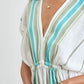 A woman wears the Lemlem Leila Plunge Dress, a hand-woven cotton dress featuring blue and green vertical stripes, a deep V-neckline, and an elastic waist. She accessorizes with a gold necklace and bracelet for chic resort style.