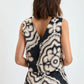 A woman with shoulder-length brown hair is seen from the back wearing the sleeveless, patterned Adowa Shell Tank by Lemlem against a plain background.