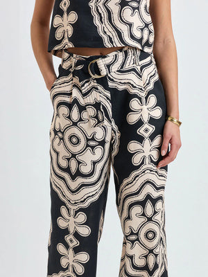 Wearing Lemlem’s Diarra Pant—black and beige patterned, relaxed straight-leg—paired with a sleeveless belted top, one hand in pocket.