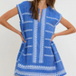 A woman wears the Lemlem Elina Caftan, a short-sleeved blue Ethiopian dress with white embroidery, split neckline, frayed hem, and hand-woven cotton.