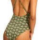 A person in Lemlem's Retiro One Piece, a green swimsuit with a palm tree pattern, crafted from premium jacquard fabric and featuring elegant cross-back straps.