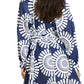 A woman wears the Lemlem Meaza Dress, featuring a blue and white pattern and long sleeves. Viewed from behind, her loose hair falls down her back as she stands with her hands at her sides.