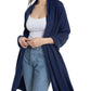 A woman, smiling with arms slightly bent, is elegantly draped in the Alashan Cashmere Cashmere Luxe Travel Wrap over a white tank top, blue open-front cardigan, and light blue jeans.