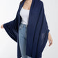 A woman stands against a plain white background wearing a white top, blue jeans, and the Alashan Cashmere Luxe Travel Wrap in navy blue.