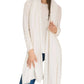 A woman stands against a white background wearing the Alashan Cashmere Cashmere Luxe Travel Wrap—a long, light cream, luxurious scarf—draped over a matching sweater and blue jeans.