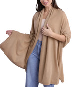 A woman styles the Alashan Cashmere Cashmere Luxe Travel Wrap in tan over a light top and blue jeans, draping one side of the wrap as if fashioning it like a luxurious scarf.