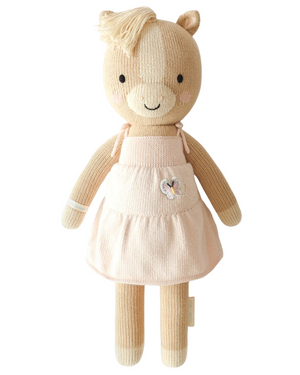 Kelsie the Pony by Cuddle + Kind is a charming 20" knitted plush doll featuring soft beige fur and a light pink dress detailed with a delicate embroidered butterfly. Standing upright against a white background, Kelsie makes an inspirational gift—perfect for anyone who wants to create something beautiful or surprise someone special with an adorable birthday plush.