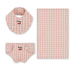 The Konges Slojd Doll Nursery Set by Konges Slojd features a pink and white checkered design on soft cotton, including a bib, diaper cover, and blanket, each featuring a cute cherry motif—ideal for your little one’s comfort!.