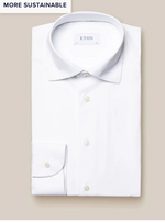 A neatly folded white Four-Way Stretch Shirt, Slim Fit by Eton with classic collar and buttoned cuffs lies on a beige background. Made from breathable tech fabric, it features a "MORE SUSTAINABLE" tag in the top left corner.