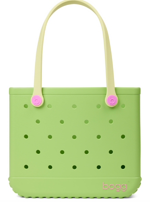 A light green Baby Bogg® Bag tote from Bogg Bags, featuring evenly spaced holes, cream-colored handles with pink accents, and the word “bogg” printed in pink in the lower corner. This durable bag is fully washable for easy care and long-lasting use.