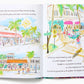 An open book with colorful Life and Lilly: A Palm Beach Adventure illustrations of a sunny Palm Beach street scene featuring buildings, palm trees, and people walking and cycling. There is text on both pages describing the vibrancy of a street. (Brand Name: Little Coconut Publication)