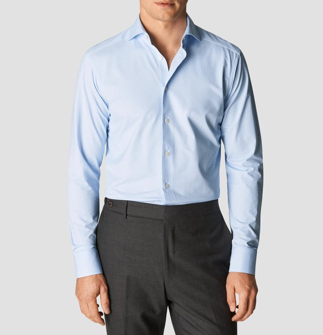 A man wearing an Eton Four-Way Stretch Shirt, Slim Fit in light blue and dark gray trousers, with the image cropped to show only his torso and lower face.