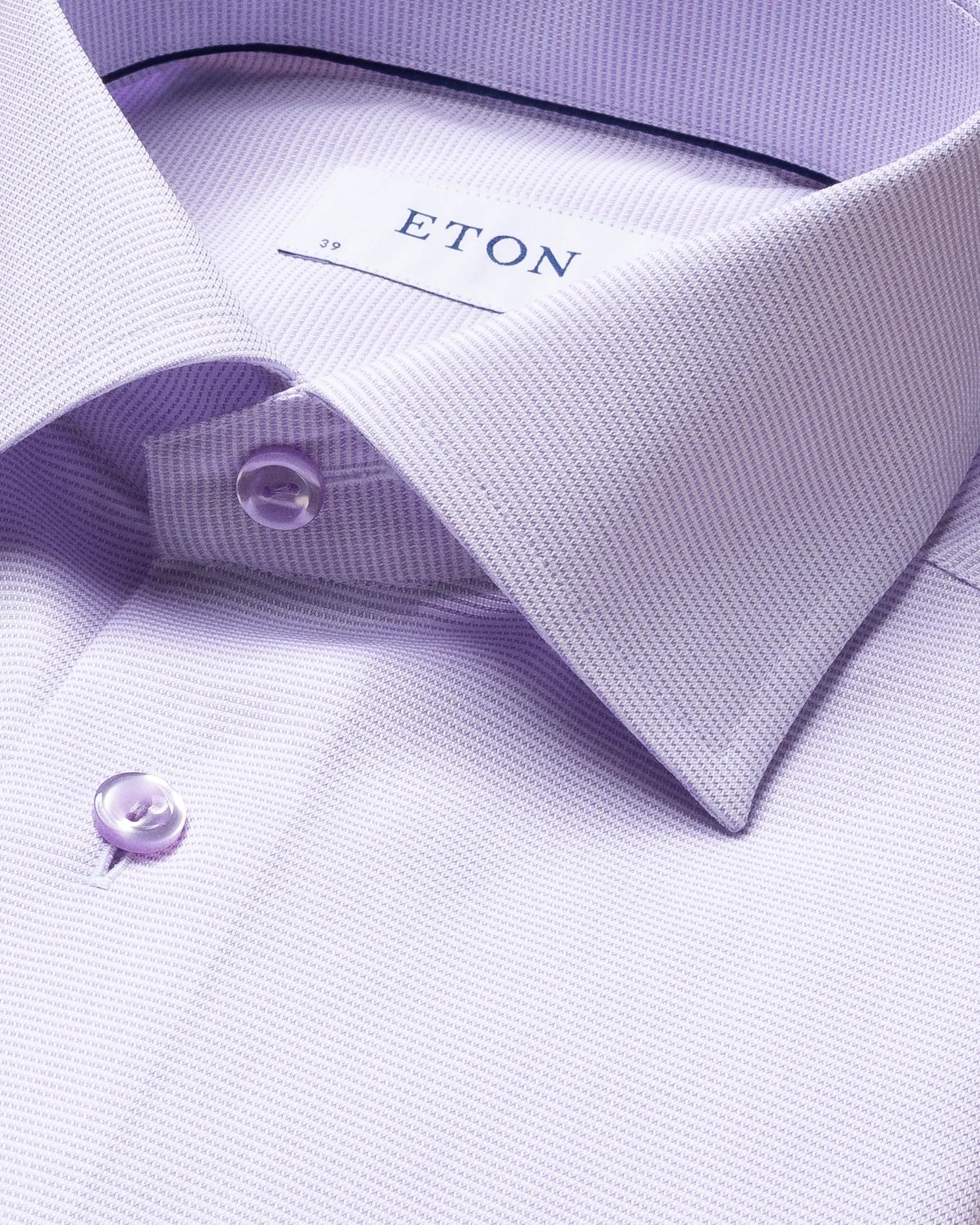 Close-up of the Eton Solid Signature Oxford Shirt in light purple cotton, featuring a button-down collar and button detailing, with the Eton brand label visible inside the collar. This crease-resistant shirt offers timeless style and easy-care convenience.