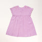 The Early Sunday Girls’ Lila Dress is a short-sleeved lilac dress featuring a pleated skirt, flutter sleeves, embroidered flowers on the shoulders, and back buttons, displayed against a light background.