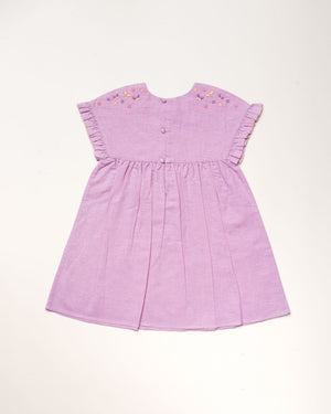 The Early Sunday Girls’ Lila Dress is a short-sleeved lilac dress featuring a pleated skirt, flutter sleeves, embroidered flowers on the shoulders, and back buttons, displayed against a light background.